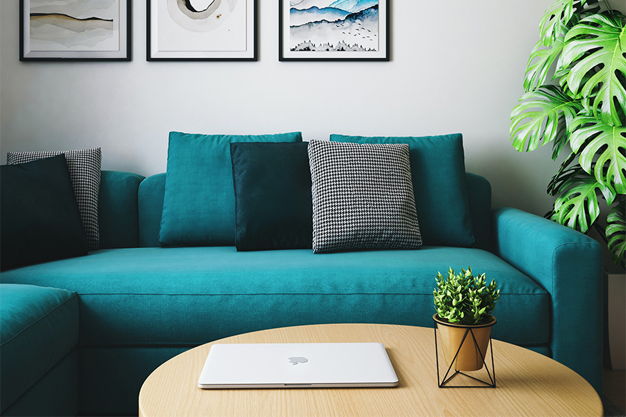 Living room with plush couch, table with computer, and potted plant.